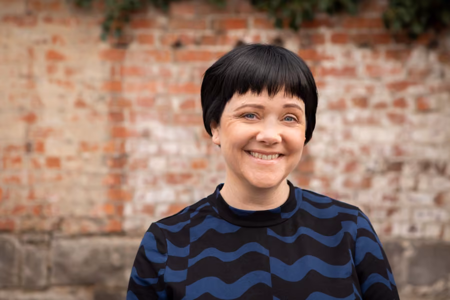 Kara is smiling at the camera in front of an out of focus background of red bricks.